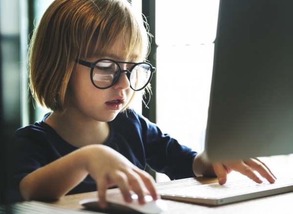 Young girl with round glasses playing on a computer