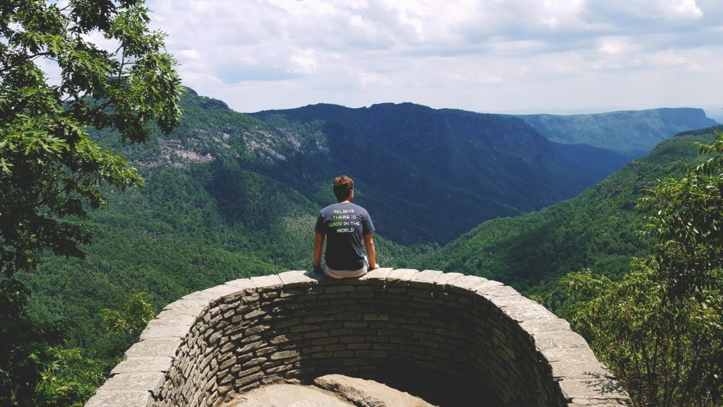 Man sitting at Blue Ridge scenic overlook with shirt that says: Believe there is good in the world