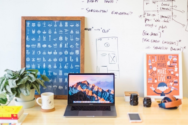 Desk with laptop, coffee mug, plant, and whiteboard with writing and drawings on it