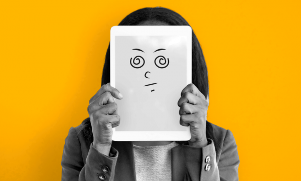 A woman holding up a whiteboard with a confused face on it.