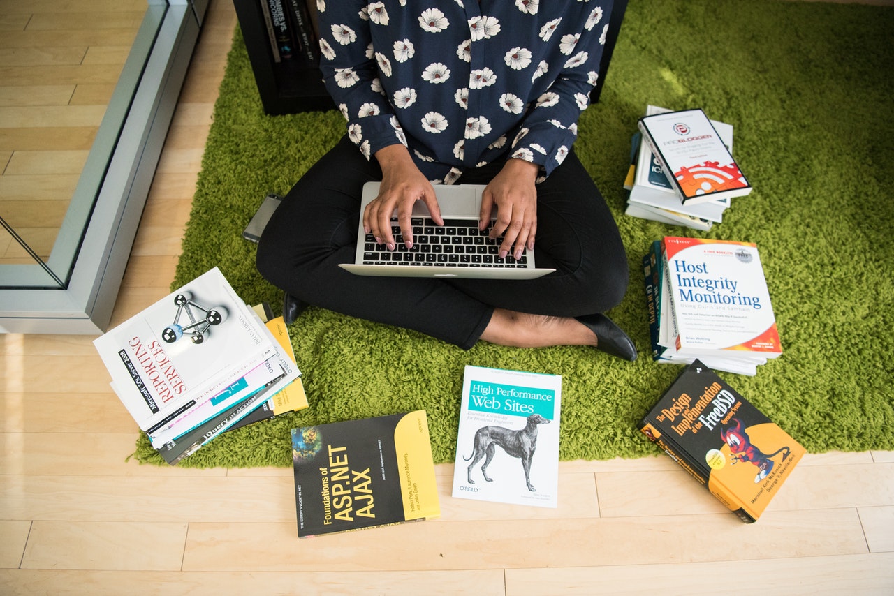A black woman typing on a laptop with books around her