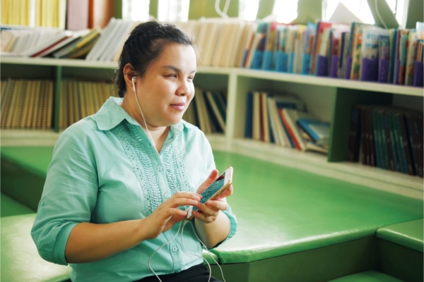 A blind woman in a green shirt uses earbuds and an iphone